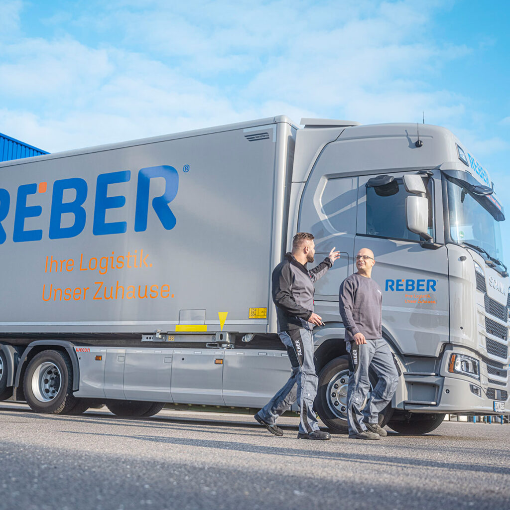 Zwei Mitarbeiter von REBER Logistik vor einem LKW - unser Kunde für Markenbildung